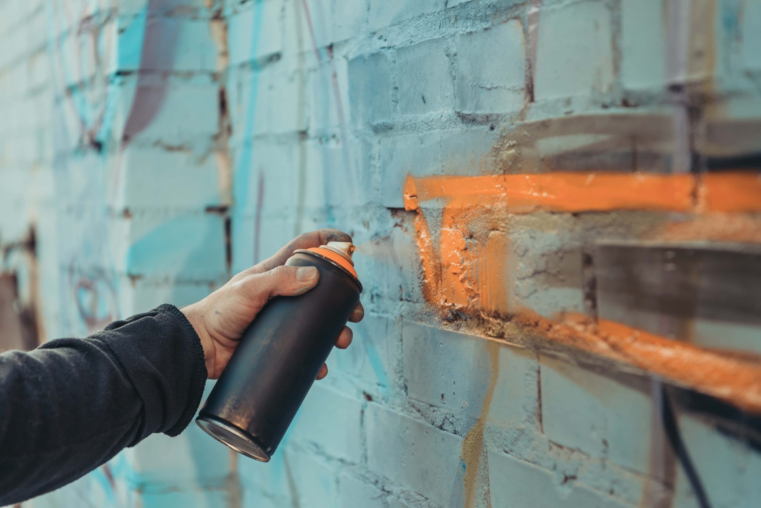 Street artist spray-painting colorful graffiti on a building wall, depicting an act that can be considered property crime or criminal mischief