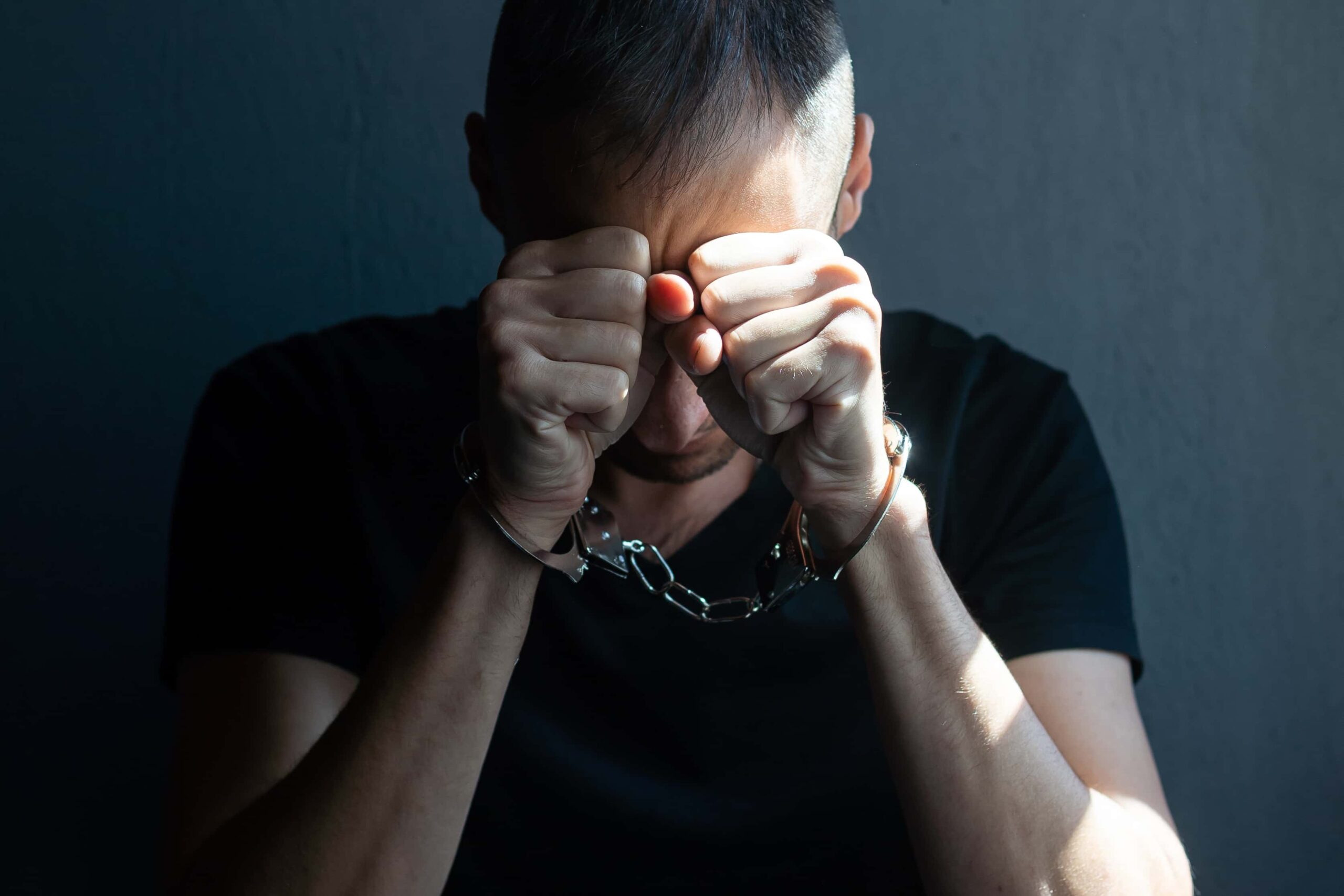 Male in handcuffs with hands covering face against a black background, symbolizing someone in need of a Long Island criminal lawyer