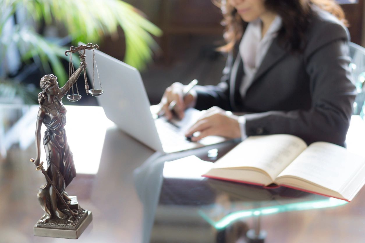 Female criminal lawyer working on laptop with Lady Justice statue on desk