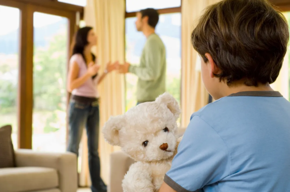 Young child holding a teddy bear while watching parents argue, illustrating emotional impact in a potential child endangerment situation