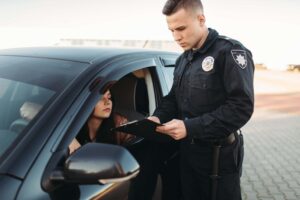 Police officer in uniform examining a female motorist’s driver's license during a traffic stop, potentially issuing a traffic violation